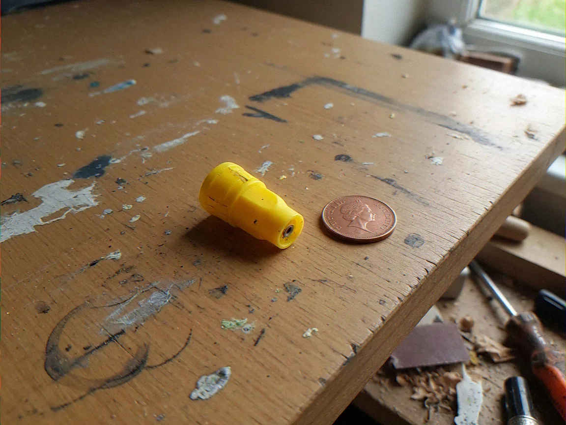 Yellow HVLP spray nozzle tip next to a UK copper coin on a DIY workbench for fence paint sprayer nozzle diameter scale